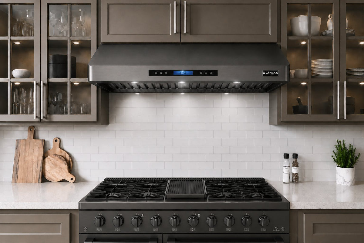 A modern Janska black gas range and stainless steel range hood installed in a contemporary kitchen with gray cabinets, white subway tile backsplash, and white countertops.