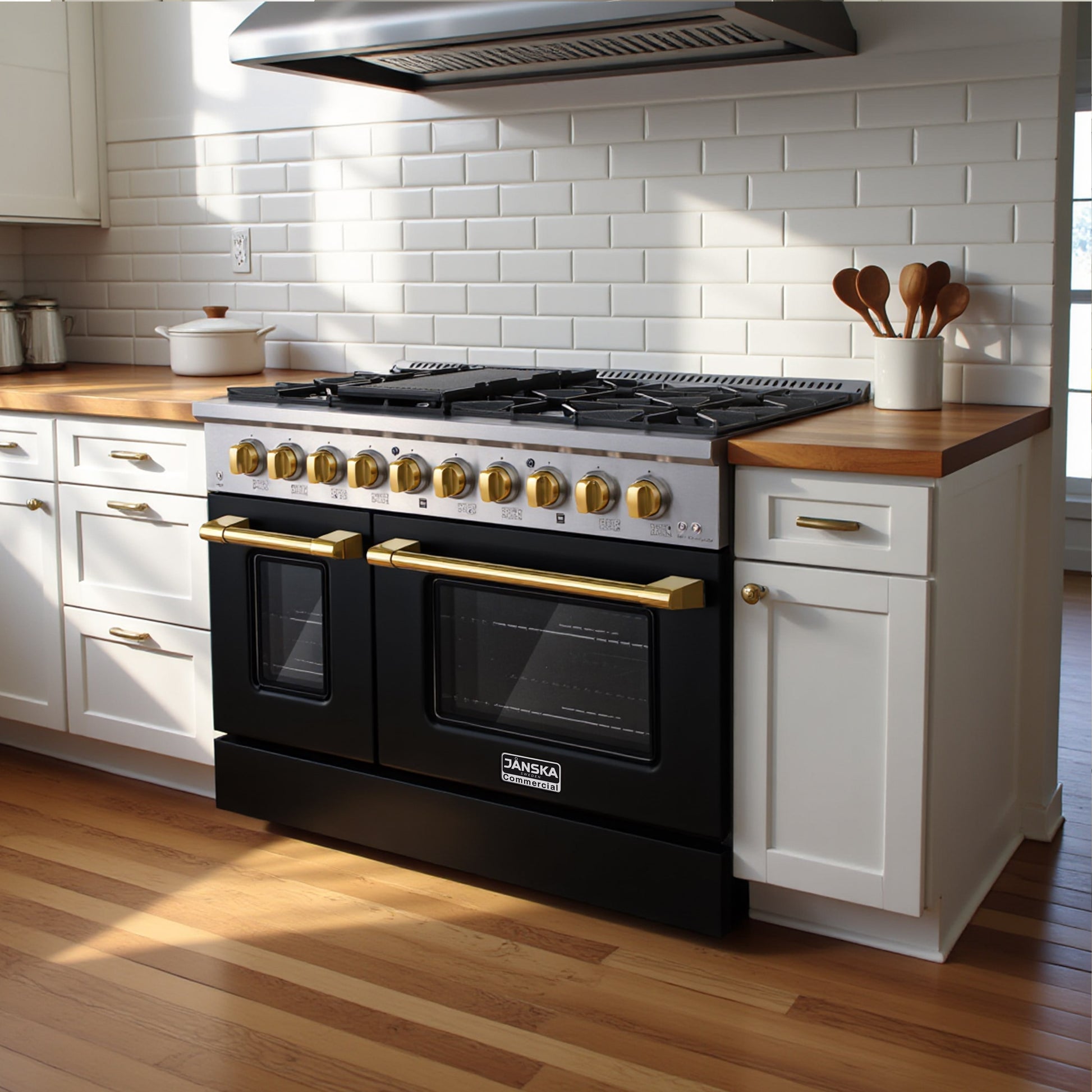 Janska black gas range in 48 inch with gold knobs and handles inset in a white classic kitchen with white cabinets, white subway tile backsplash, wooden floors and rangehood. 