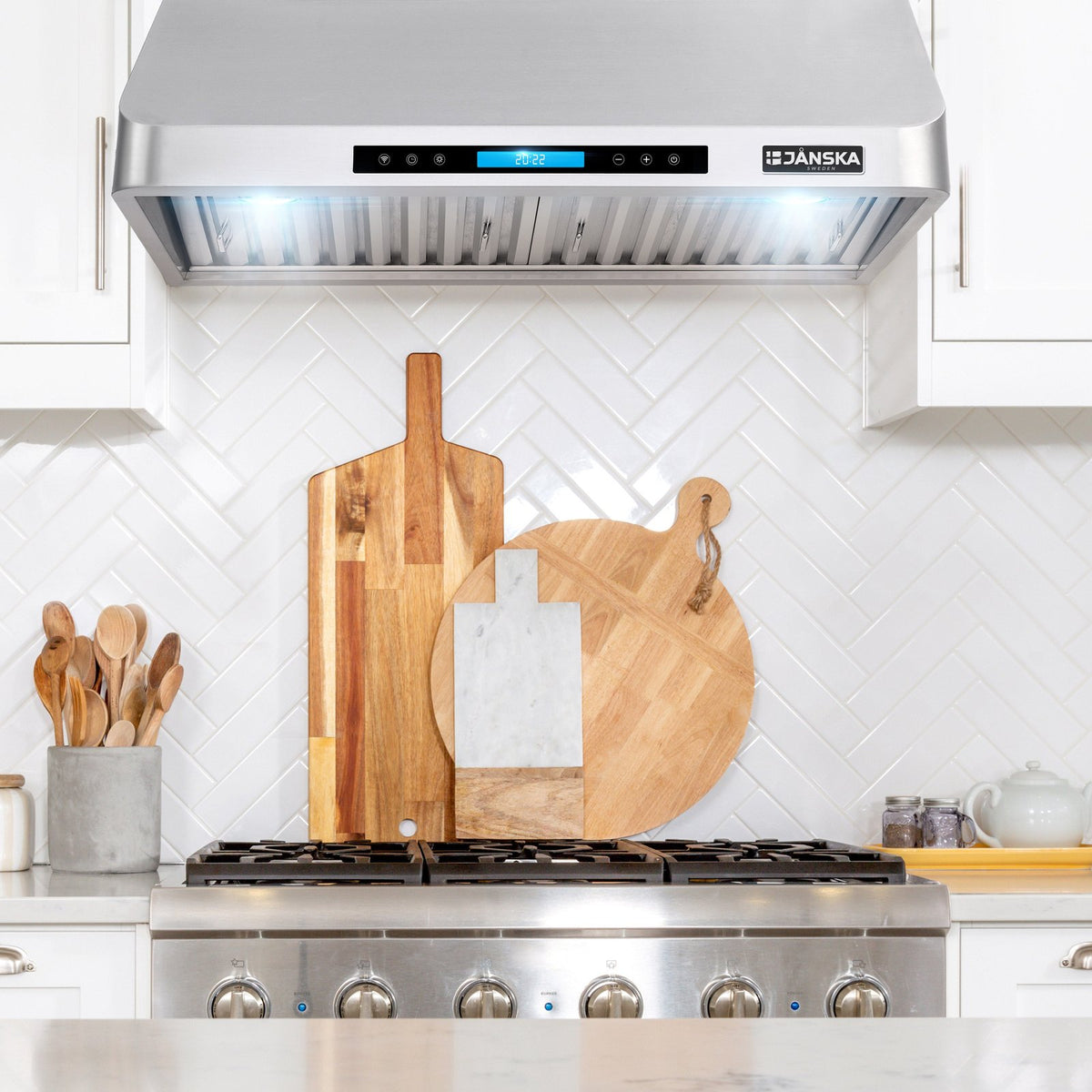 Janska range hood above a stove with wooden cutting boards on the stove. 