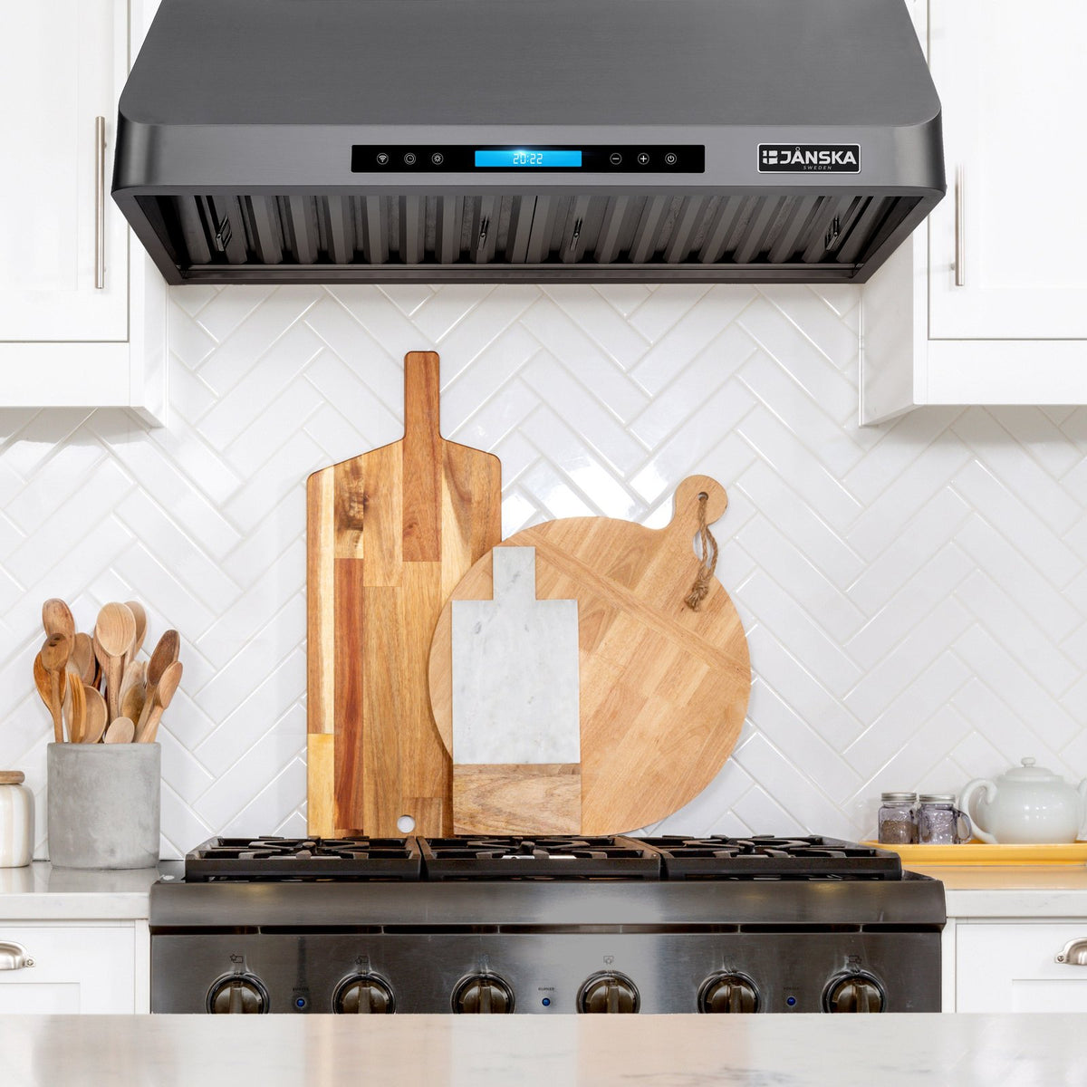 Janska range hood above a stove with wooden cutting boards on the stove. 