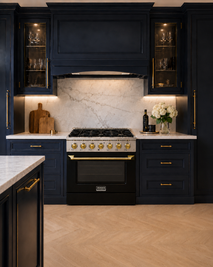 Modern blue kitchen with black cabinets, marble backsplash, and gold hardware. Janska black gas range with gold handle and gold knob.