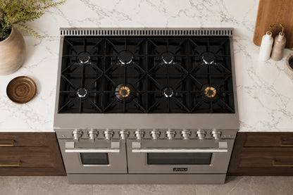 A top-down view of a Janska stainless steel and black gas range with eight burners and two oven doors, set into a modern kitchen with a white marble countertop and dark wood cabinets.