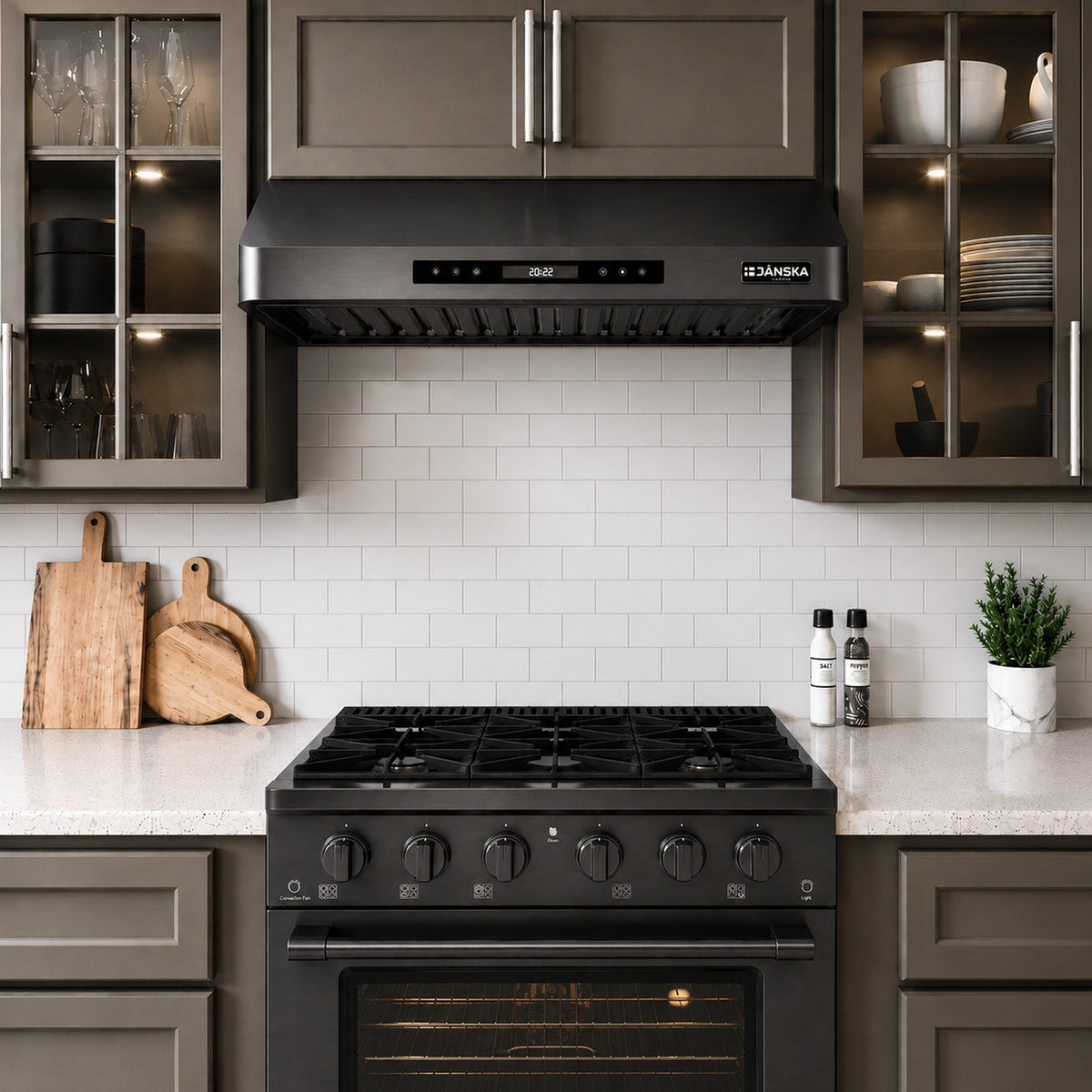 A Janska 36 inch black gas range with a matching range hood and oven, set in a modern kitchen with gray cabinets, white subway tile backsplash, and marble countertops.